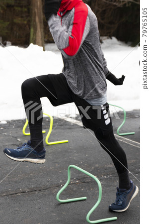 Runner stepping over mini hurdles in a parking lot because of a snow storm 79765105