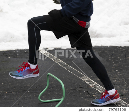 Runner stepping over mini hurdles in a parking lot with snow in the background Runner stepping over mini hurdles in a parking lot with snow in the background 79765106