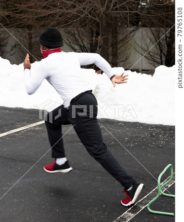 Fast runner running over mini hurdles in a parking lot with snow 79765108
