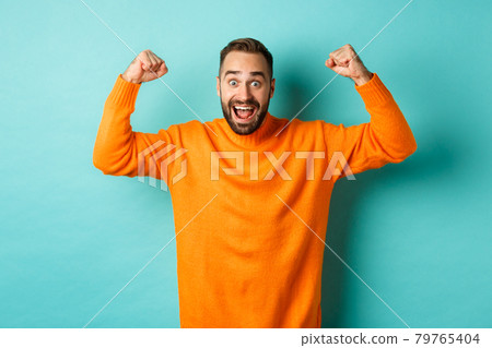 Handsome man celebrating victory, winning and looking happy, triumphing over win, standing over light blue background Handsome man celebrating victory, winning and looking happy, triumphing over win, standing over light blue background 79765404