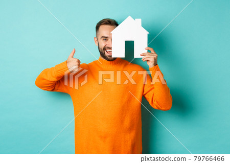 Real estate concept. Satisfied man recommending agency, showing thumb up and house maket, standing over blue background 79766466