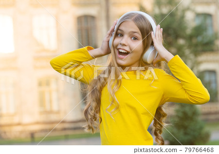Girl listening music modern gadget. Kid happy with wireless headset outdoors Girl listening music modern gadget. Kid happy with wireless headset outdoors 79766468