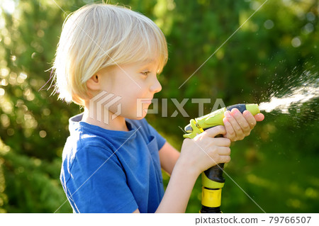 Funny little boy watering plants and playing with garden hose with sprinkler in sunny backyard. Preschooler child having fun with spray of water. Summer outdoors activity for kids. Happy childhood. Funny little boy watering plants and playing with garden hose with sprinkler in sunny backyard. Preschooler child having fun with spray of water. Summer outdoors activity for kids. Happy childhood. 79766507