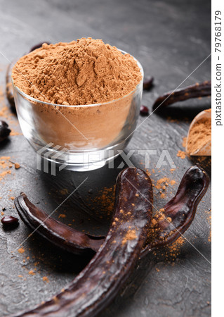 Dry carob pods and carob powder over dark background Dry carob pods and carob powder over dark background 79768179