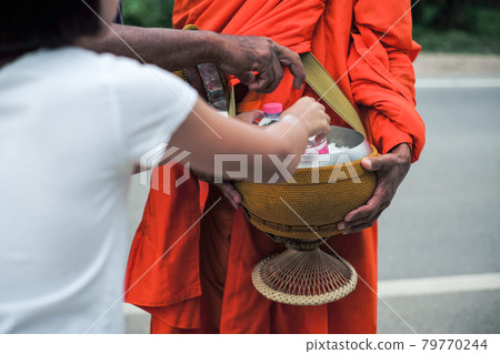 Rear view of girl puts the food into the bowl of monk during making the merit 79770244