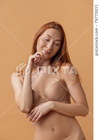Young beautiful redheaded woman in lingerie posing isolated over sand color studio back ground. The fitness, diet, sports, natural beauty and aesthetic cosmetology concept. Young beautiful redheaded woman in lingerie posing isolated over sand color studio back ground. The fitness, diet, sports, natural beauty and aesthetic cosmetology concept. 79770831