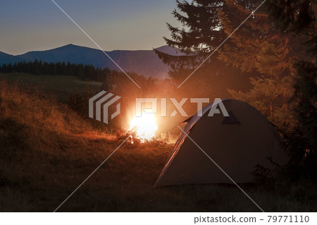Hikers tent in mountains at evening with a bonfire with sparkles near it Hikers tent in mountains at evening with a bonfire with sparkles near it 79771110