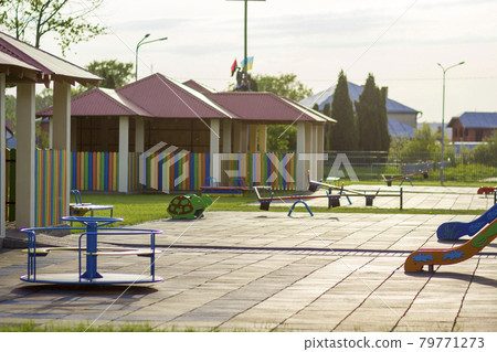 Beautiful new modern playground in kindergarten with soft pavement, bright new multicolored alcoves, swings, slides, benches, roundabout and sandbox. Perfect place for children activities outdoors. Beautiful new modern playground in kindergarten with soft pavement, bright new multicolored alcoves, swings, slides, benches, roundabout and sandbox. Perfect place for children activities outdoors. 79771273