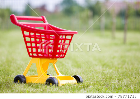 Bright plastic colorful shopping cart toy outdoors on sunny summer day. 79771713