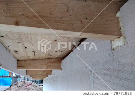 Installation of wooden beams of roof frame with spray foam on a house wall under construction. 79771958
