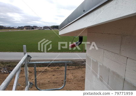 Building fasade under construction with unfinished wall and wooden roof boards with plastic gutter pipes. 79771959