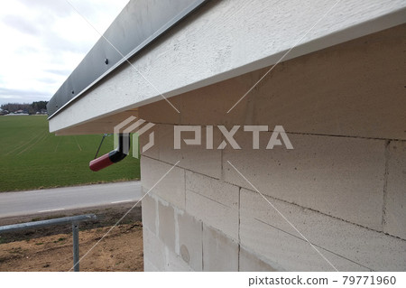 Building fasade under construction with unfinished wall and wooden roof boards with plastic gutter pipes. Building fasade under construction with unfinished wall and wooden roof boards with plastic gutter pipes. 79771960