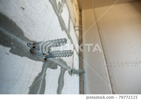 Unfinished brick wall in a room under construction prepared for drywall plates frame installation. Unfinished brick wall in a room under construction prepared for drywall plates frame installation. 79772115