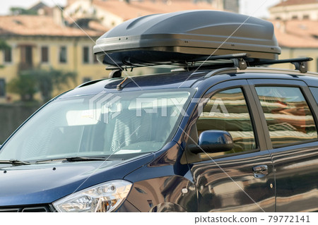 A car with roof baggage trunk parked on the side of the street on a parking lot. 79772141