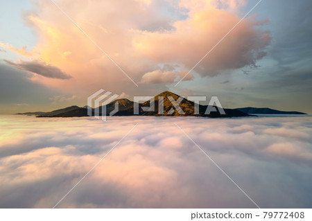 Aerial view of a big mountain over white dense clouds at bright sunrise. 79772408