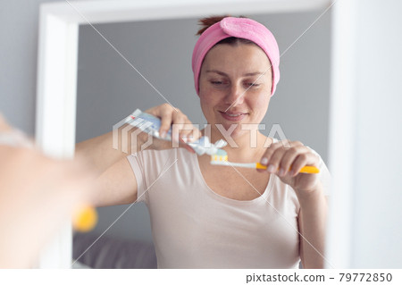 Happy smile woman brushing teeth squeezing mint toothpaste on plastic toothbrush, taking care about fresh breath and caries prevention. 79772850