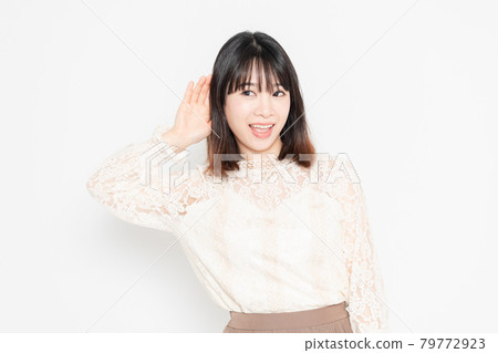 一個穿著蕾絲上衣的年輕女子站在白色背景前傾聽 一個穿著蕾絲上衣的年輕女子站在白色背景前傾聽 79772923