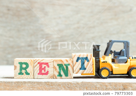 Toy forklift hold letter block t to complete word rent on wood background Toy forklift hold letter block t to complete word rent on wood background 79773303