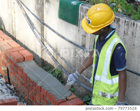 KUALA LUMPUR, MALAYSIA -JULY 14, 2016: Construction workers laying clay bricks at the construction site to form a wall. The brick stick together using the cement mortar. KUALA LUMPUR, MALAYSIA -JULY 14, 2016: Construction workers laying clay bricks at the construction site to form a wall. The brick stick together using the cement mortar. 79773528