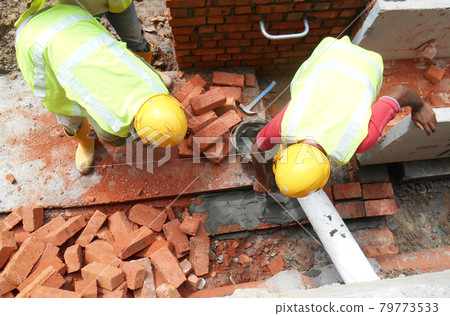 KUALA LUMPUR, MALAYSIA -JULY 14, 2016: Construction workers laying clay bricks at the construction site to form a wall. The brick stick together using the cement mortar. KUALA LUMPUR, MALAYSIA -JULY 14, 2016: Construction workers laying clay bricks at the construction site to form a wall. The brick stick together using the cement mortar. 79773533