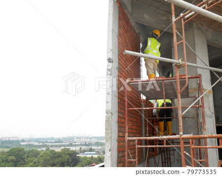 KUALA LUMPUR, MALAYSIA -JULY 14, 2016: Construction workers laying clay bricks at the construction site to form a wall. The brick stick together using the cement mortar. KUALA LUMPUR, MALAYSIA -JULY 14, 2016: Construction workers laying clay bricks at the construction site to form a wall. The brick stick together using the cement mortar. 79773535