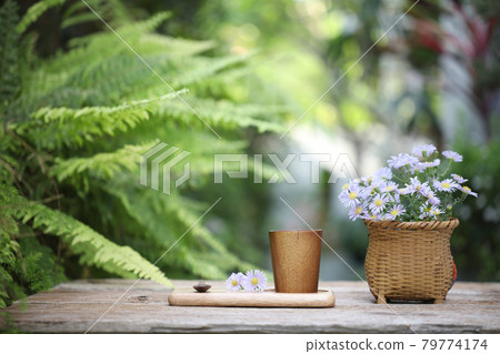 Wooden cup on wooden plate with purple aster flowers on wooden table and fern leaves  Wooden cup on wooden plate with purple aster flowers on wooden table and fern leaves  79774174