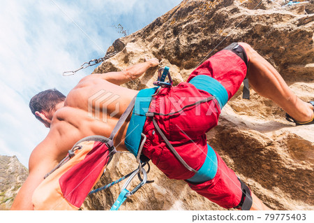 Close-up view from below of the back of a man climbing a rock. Close-up view from below of the back of a man climbing a rock. 79775403