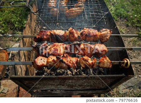 Barbeque meat and sausages or bratwurst on a grill grate in backyard. Man preparing shashlik or shish kebab over charcoal. Grilled meat on metal skewer outdoor. BBQ party or picnic food. Close up shot 79776616