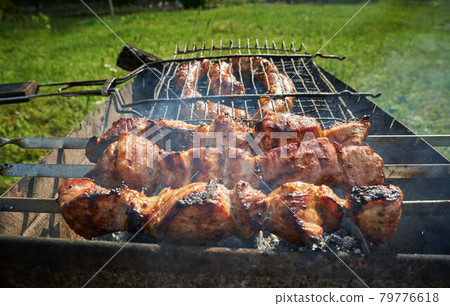 Barbeque meat and sausages or bratwurst on a grill grate in backyard. Man preparing shashlik or shish kebab over charcoal. Grilled meat on metal skewer outdoor. BBQ party or picnic food. Close up shot 79776618