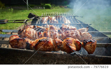 Barbeque meat and sausages or bratwurst on a grill grate in backyard. Man preparing shashlik or shish kebab over charcoal. Grilled meat on metal skewer outdoor. BBQ party or picnic food. Close up shot 79776619