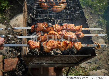Barbeque meat and sausages or bratwurst on a grill grate in backyard. Man preparing shashlik or shish kebab over charcoal. Grilled meat on metal skewer outdoor. BBQ party or picnic food. Close up shot 79776635