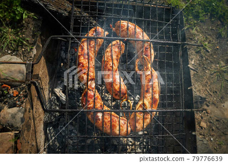 Barbeque meat and sausages or bratwurst on a grill grate in backyard. Man preparing shashlik or shish kebab over charcoal. Grilled meat on metal skewer outdoor. BBQ party or picnic food. Close up shot 79776639