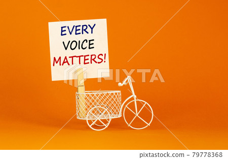 Wooden clothespin with white sheet of paper. Text 'every voice matters'. Miniature bicycle model. Beautiful orange background. Business concept, copy space. 79778368