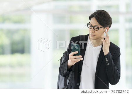 一個三十多歲的男人戴著耳機，看著智能手機屏幕的休閒商業形象 79782742