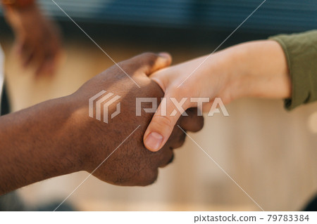 Close-up top view of handshake of Caucasian woman and black male indoors at home office, selective focus. 79783384