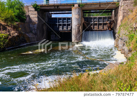 Flowing water with water spray from the open sluice gates of a small dam 79787477