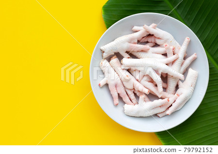 Raw chicken feet in white plate on yellow with banana leaf background. 79792152