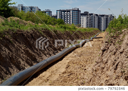 A large pipe lies in the trench. Water routing to the new house. house with water. residential complex A large pipe lies in the trench. Water routing to the new house. house with water. residential complex 79792846