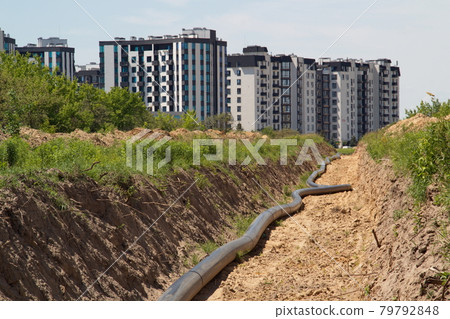 A large pipe lies in the trench. Water routing to the new house. house with water. residential complex A large pipe lies in the trench. Water routing to the new house. house with water. residential complex 79792848