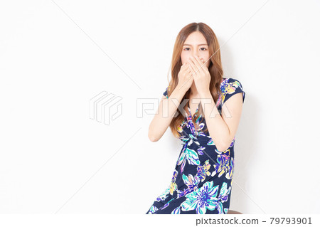 A young woman in a blue one-piece, hiding her mouth in front of a white wall 79793901
