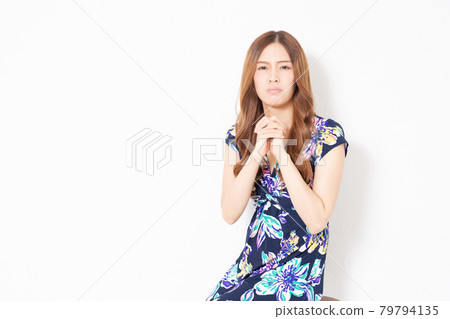 A young woman in a blue one-piece, making a request gesture in front of a white wall 79794135