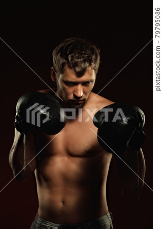 This is a dramatic portrait of a boxer in old boxing gloves on a dark background. An athletic mixed 79795086
