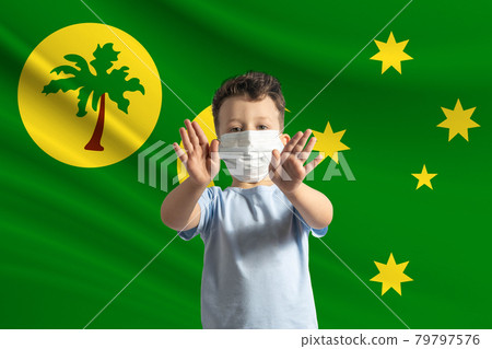 Little white boy in a protective mask on the background of the flag of Cocos Islands. Makes a stop sign with his hands, stay at home Cocos Islands 79797576