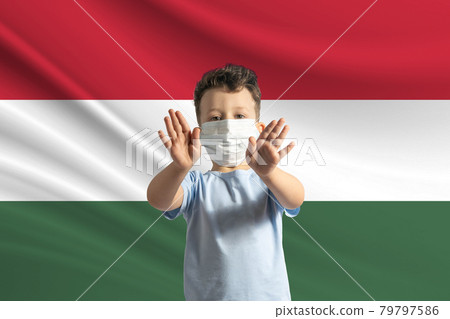 Little white boy in a protective mask on the background of the flag of Hungary. Makes a stop sign with his hands, stay at home Hungary 79797586