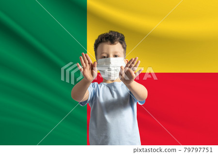 Little white boy in a protective mask on the background of the flag of Benin. Makes a stop sign with his hands, stay at home Benin Little white boy in a protective mask on the background of the flag of Benin. Makes a stop sign with his hands, stay at home Benin 79797751