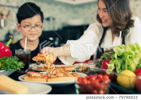 Asian mom and son sitting in home kitchen and eating homemade pizza together with various kinds of vegetables. Idea for happiness of good time sharing in family Asian mom and son sitting in home kitchen and eating homemade pizza together with various kinds of vegetables. Idea for happiness of good time sharing in family 79798833
