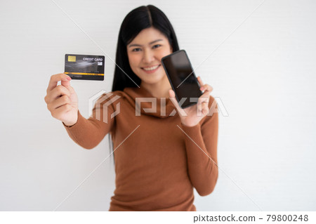 Happy Asian woman holding card credit and smartphone for mobile banking on the internet. Concept of new lifestyle and financing technology. Happy Asian woman holding card credit and smartphone for mobile banking on the internet. Concept of new lifestyle and financing technology. 79800248