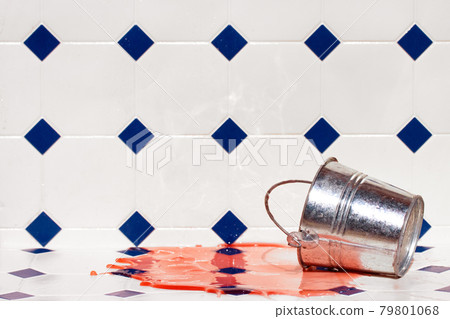 A colored liquid flows out of a metal bucket on a white tiles. 79801068