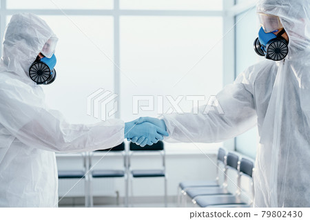 two of the laboratory staff in protective suits shaking hands with each other. 79802430