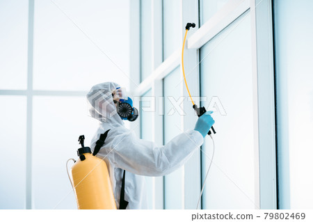 disinfector in a protective suit is spraying a disinfectant in the room. disinfector in a protective suit is spraying a disinfectant in the room. 79802469